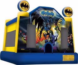 A colorful, Batman-themed inflatable bounce house features comic book-style Batman graphics, with two Batman logos on top and mesh windows on the sides. The structure is mainly blue and yellow.