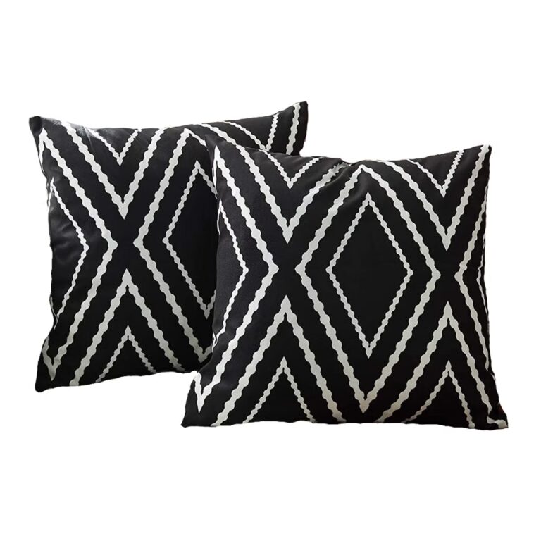 Two square throw pillows with a black background and bold white geometric diamond patterns. The pillows are placed at an angle against a plain white backdrop.