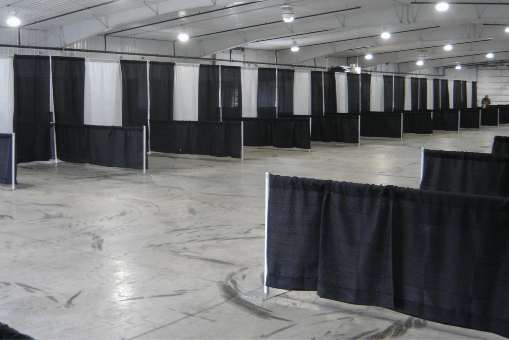 A large indoor space with high ceilings, divided by black and white curtains on metal frames into sections or booths. The concrete floor has tire marks, and few people are present—perfect for exploring unique holiday party ideas in a versatile venue.